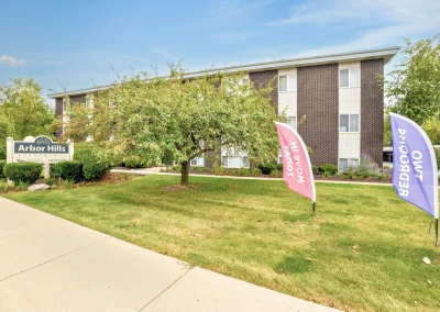 Exterior view of Arbor Hills Apartments showing landscaped grounds and residential buildings along the sidewalk